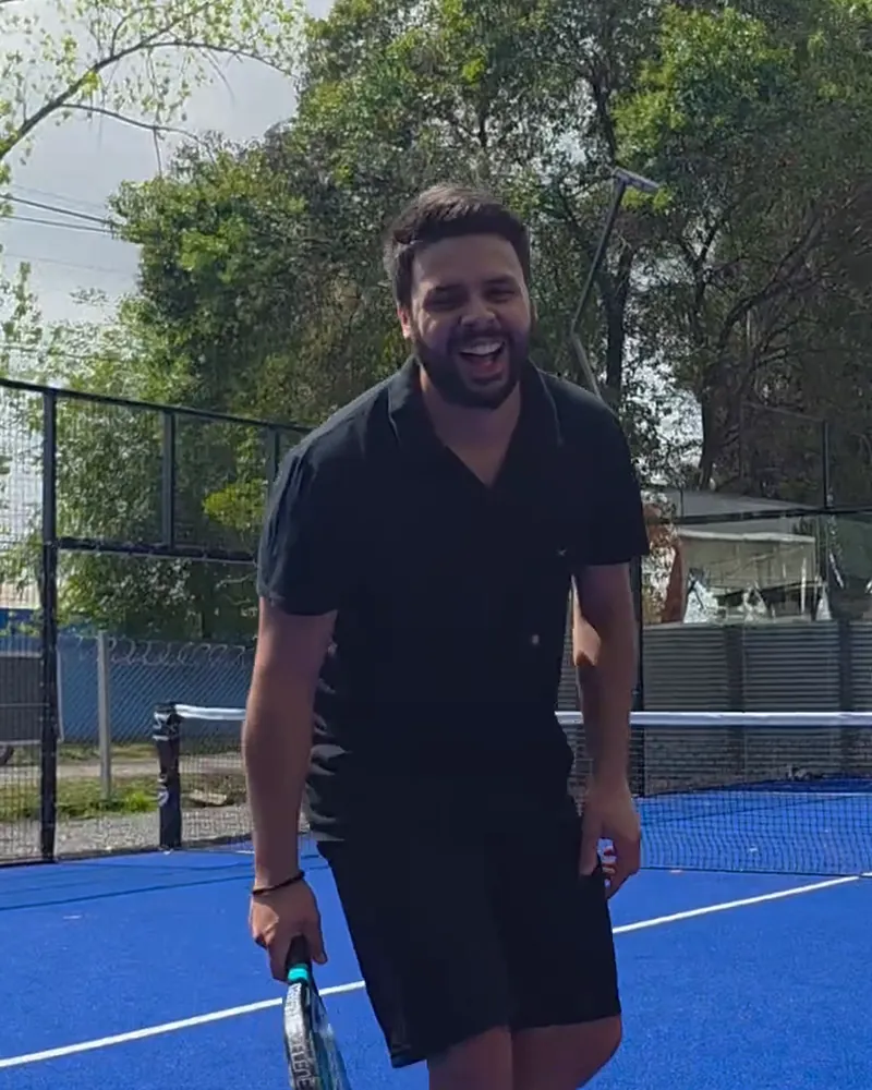 El profe se ríe en la cancha azul con la paleta en la mano